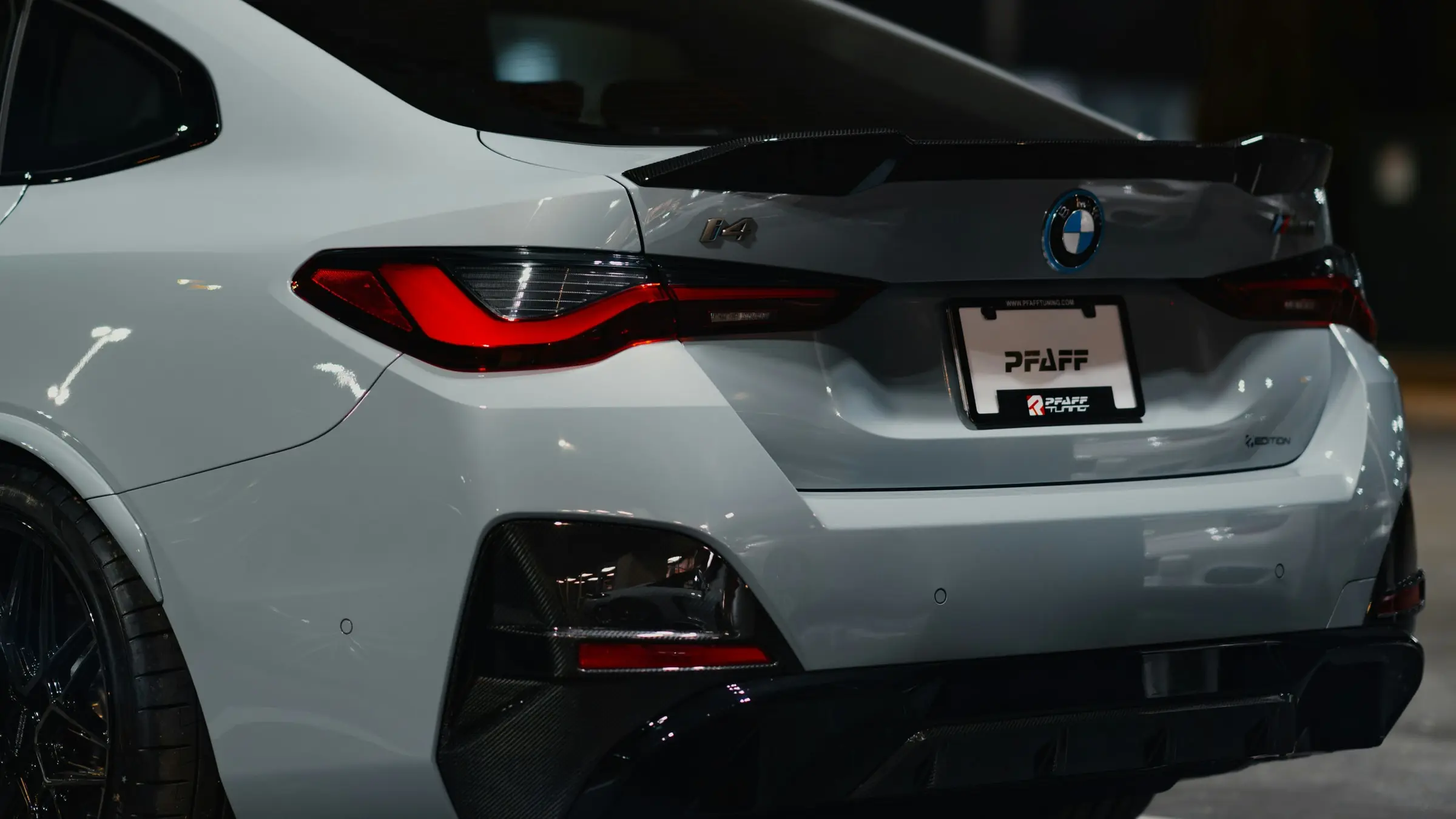 The rear of a white BMW i4 with a carbon-fibre spoiler, parked under lights at night