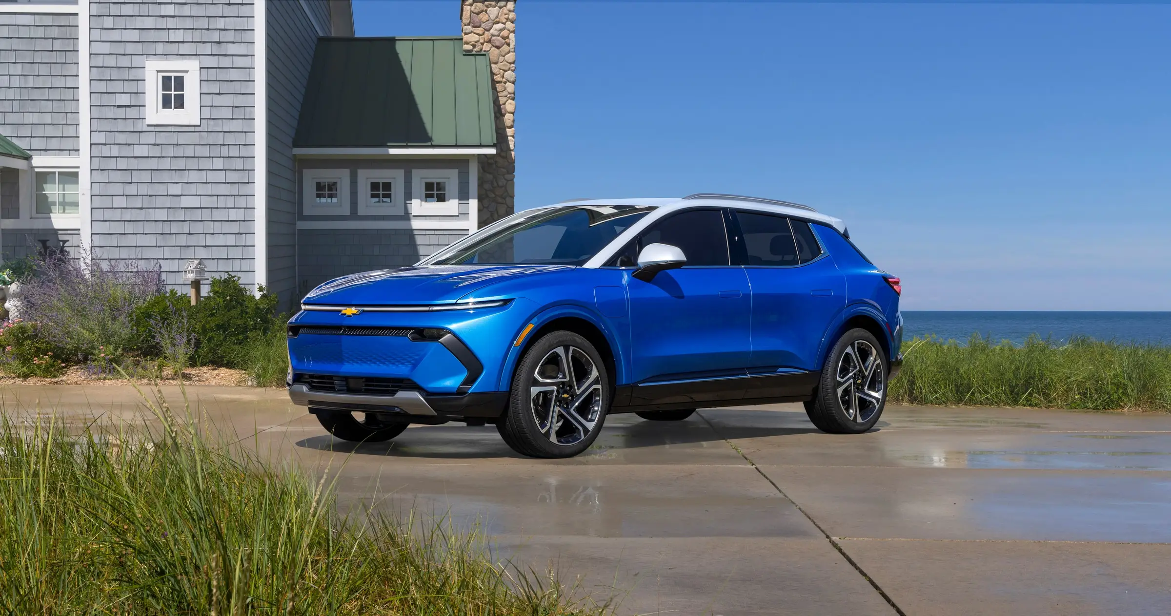 A blue Chevrolet Equinox EV parked beside a house near the water