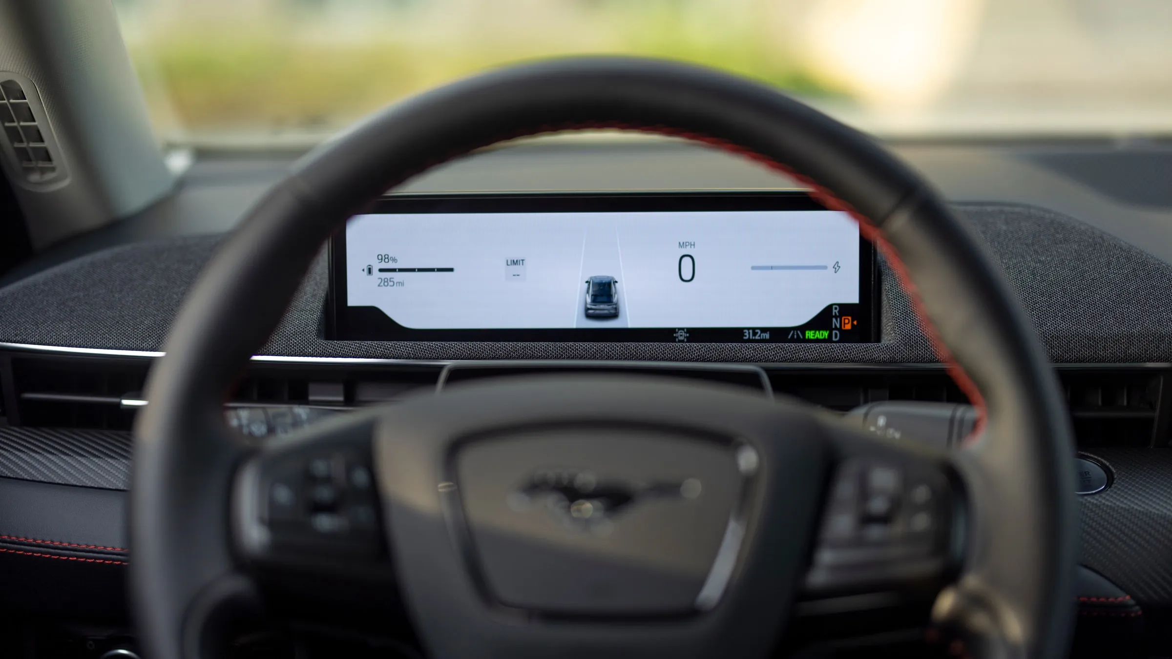A Ford Mustang Mach-E's digital instrument cluster seen through the steering wheel, reading 98% charge and 285 miles of range