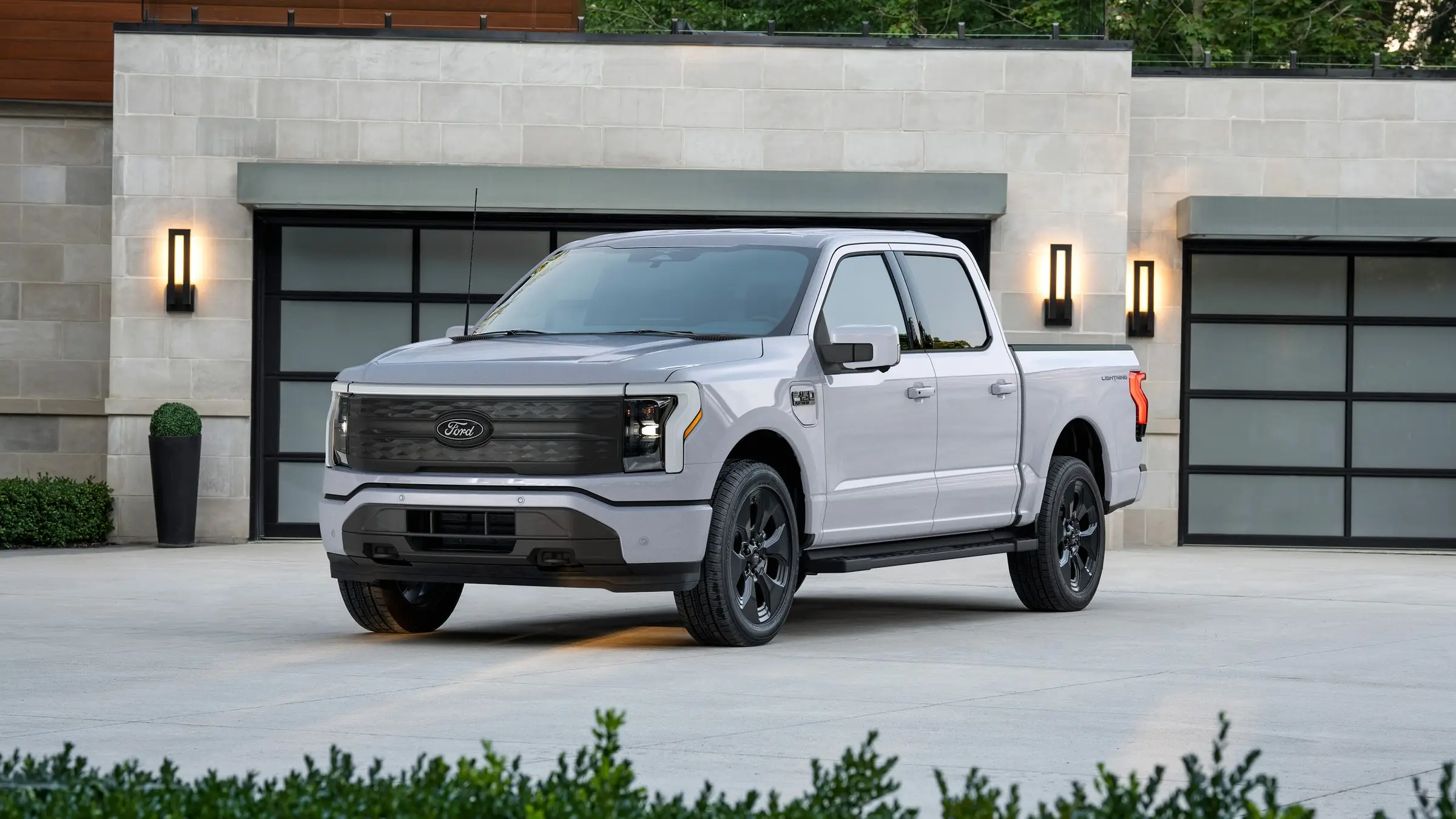 A white Ford F-150 Lightning Platinum parked on a concrete forecourt in front of a stone house with glass garage doors