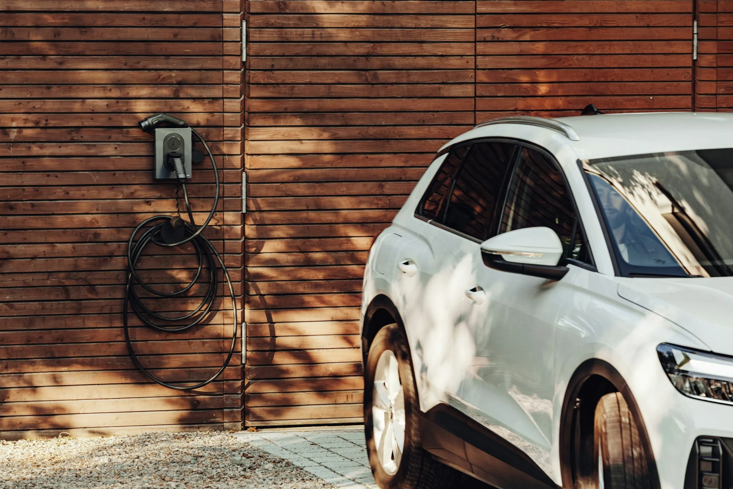 A wall-mounted home charger beside a parked electric car on a driveway