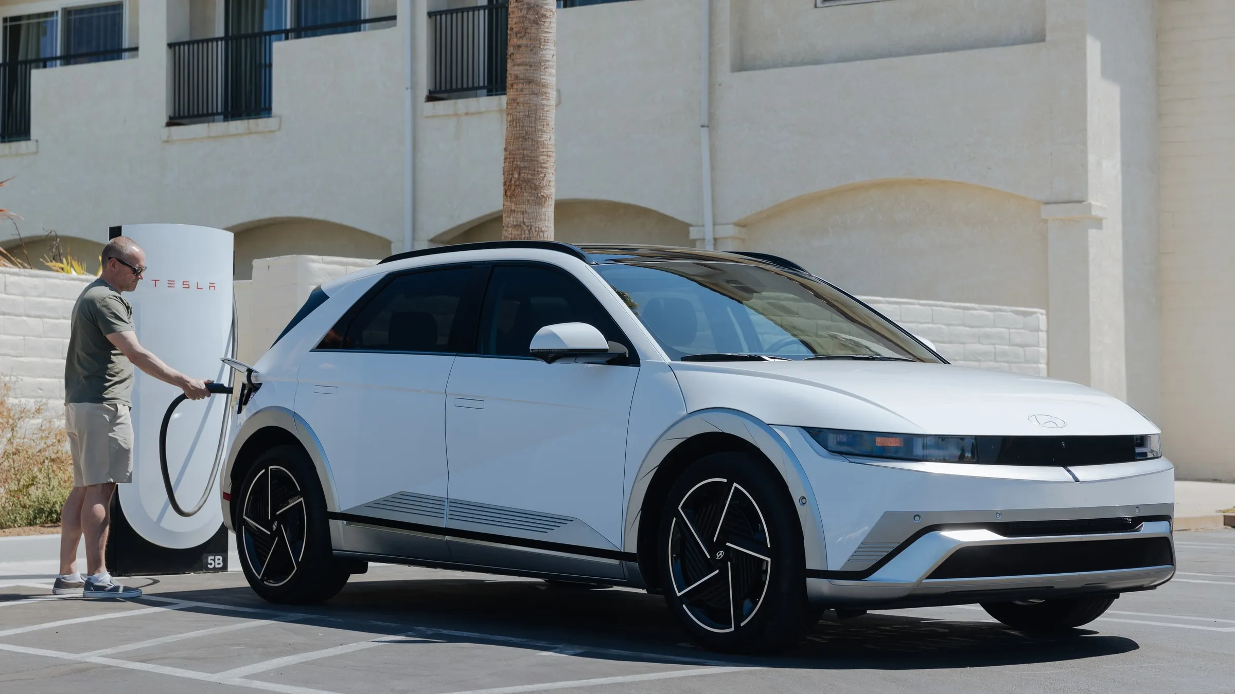 A man plugs a white Hyundai Ioniq 5 into a Tesla Supercharger stall