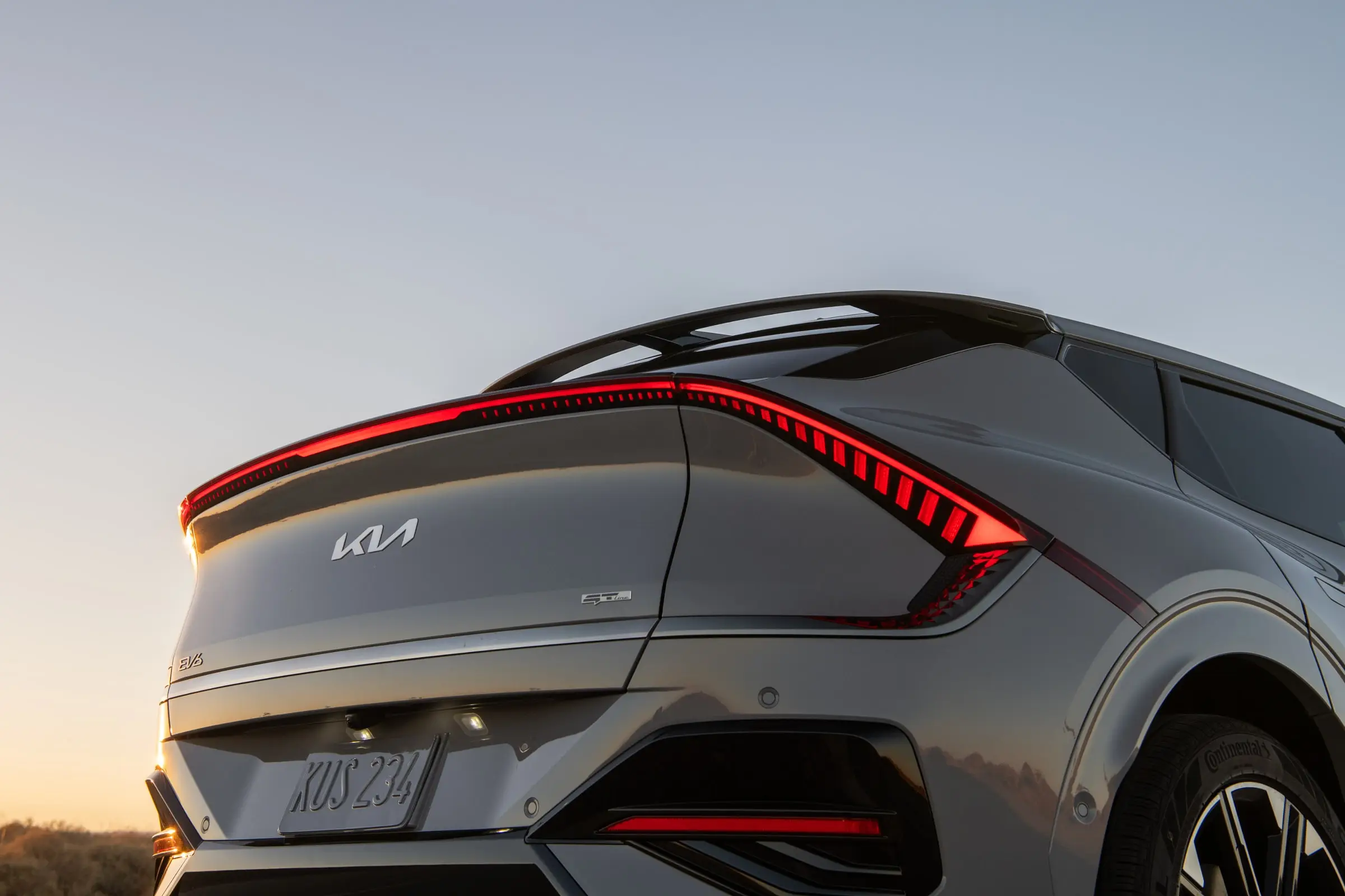 A grey Kia EV6 seen from the rear three-quarter at sunset