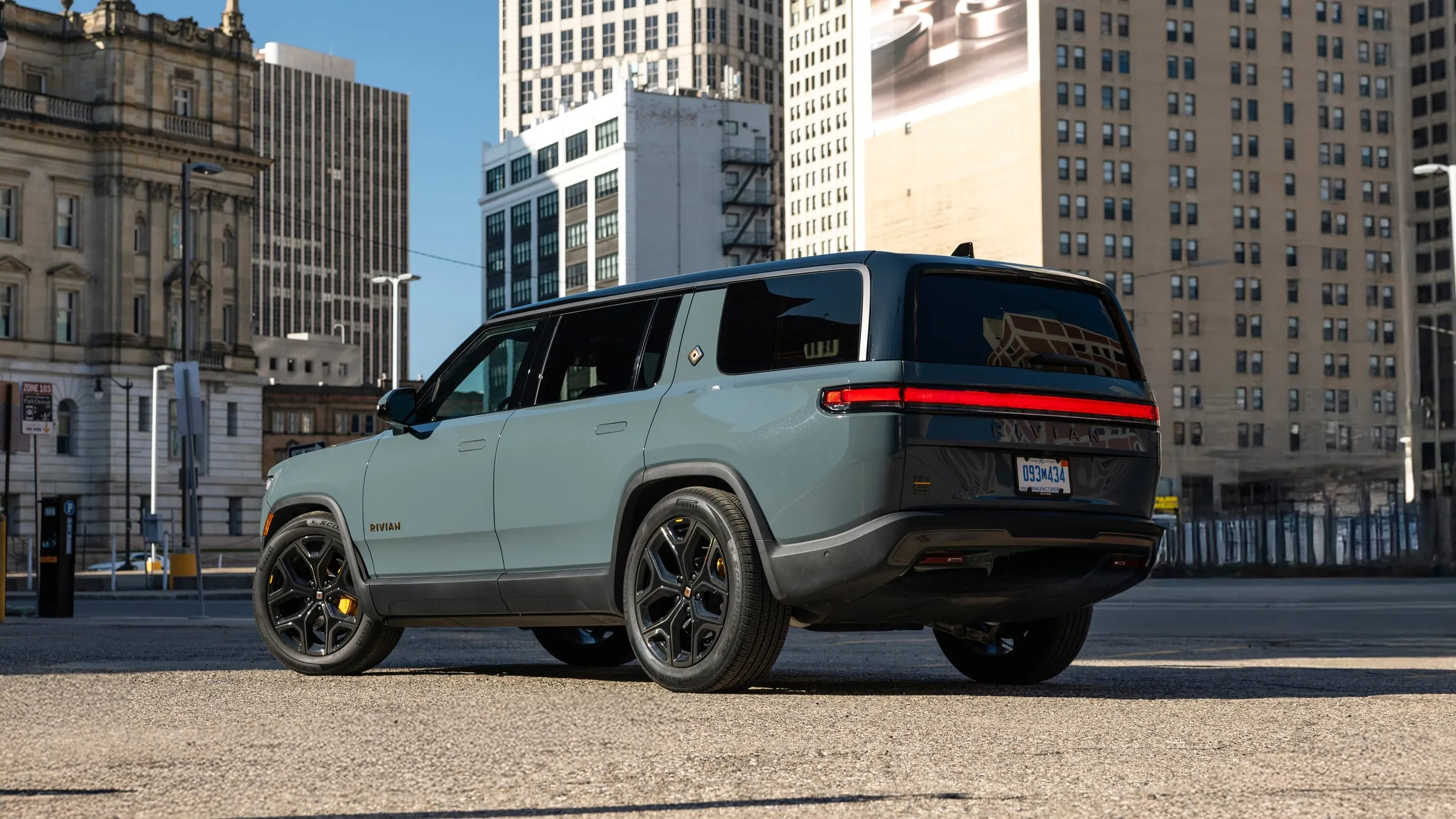 A Rivian R1S seen from the rear three-quarter, with downtown Detroit towers behind it