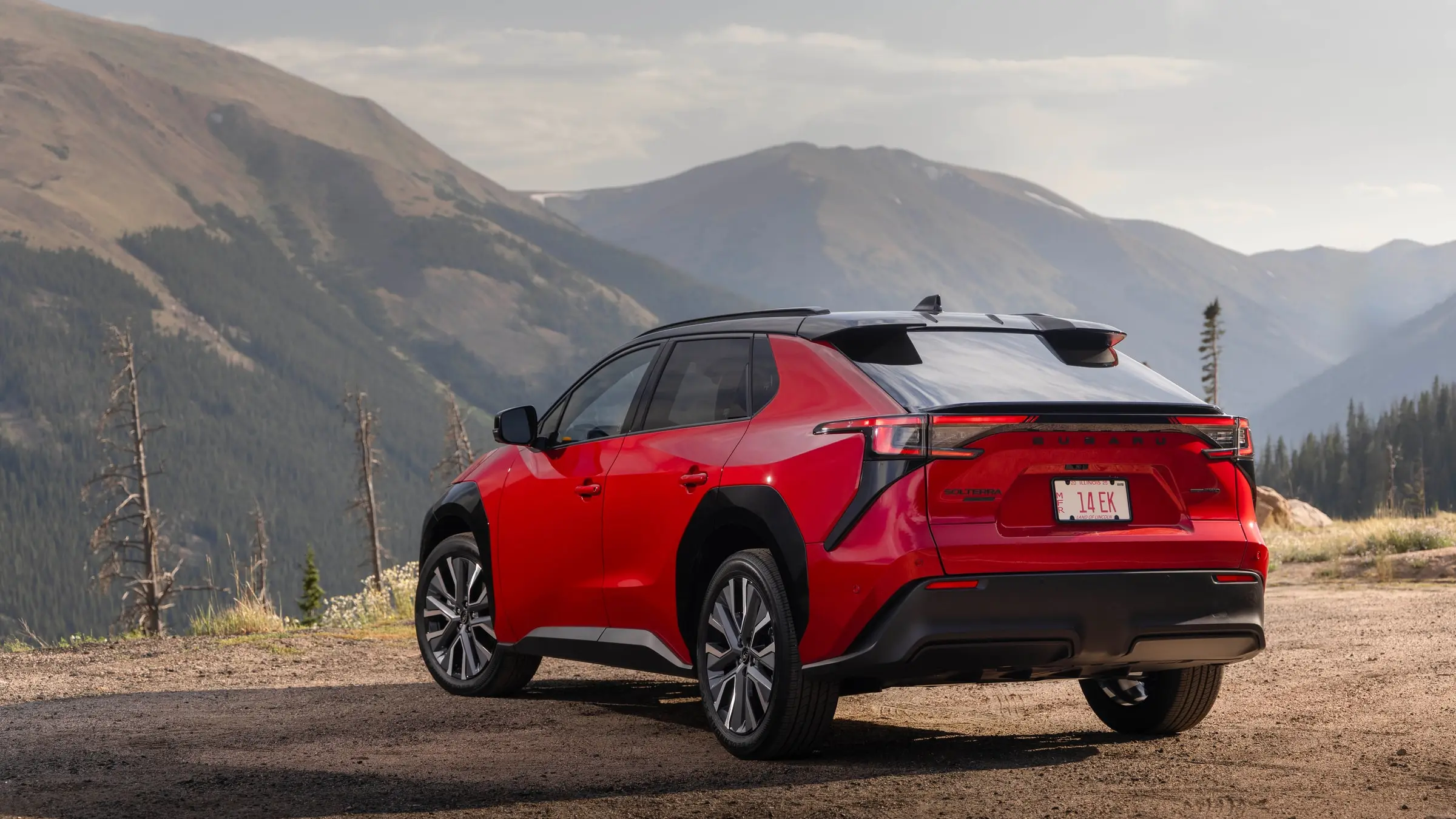 A red 2026 Subaru Solterra seen from the rear three-quarter on a gravel pull-off with forested mountains behind it